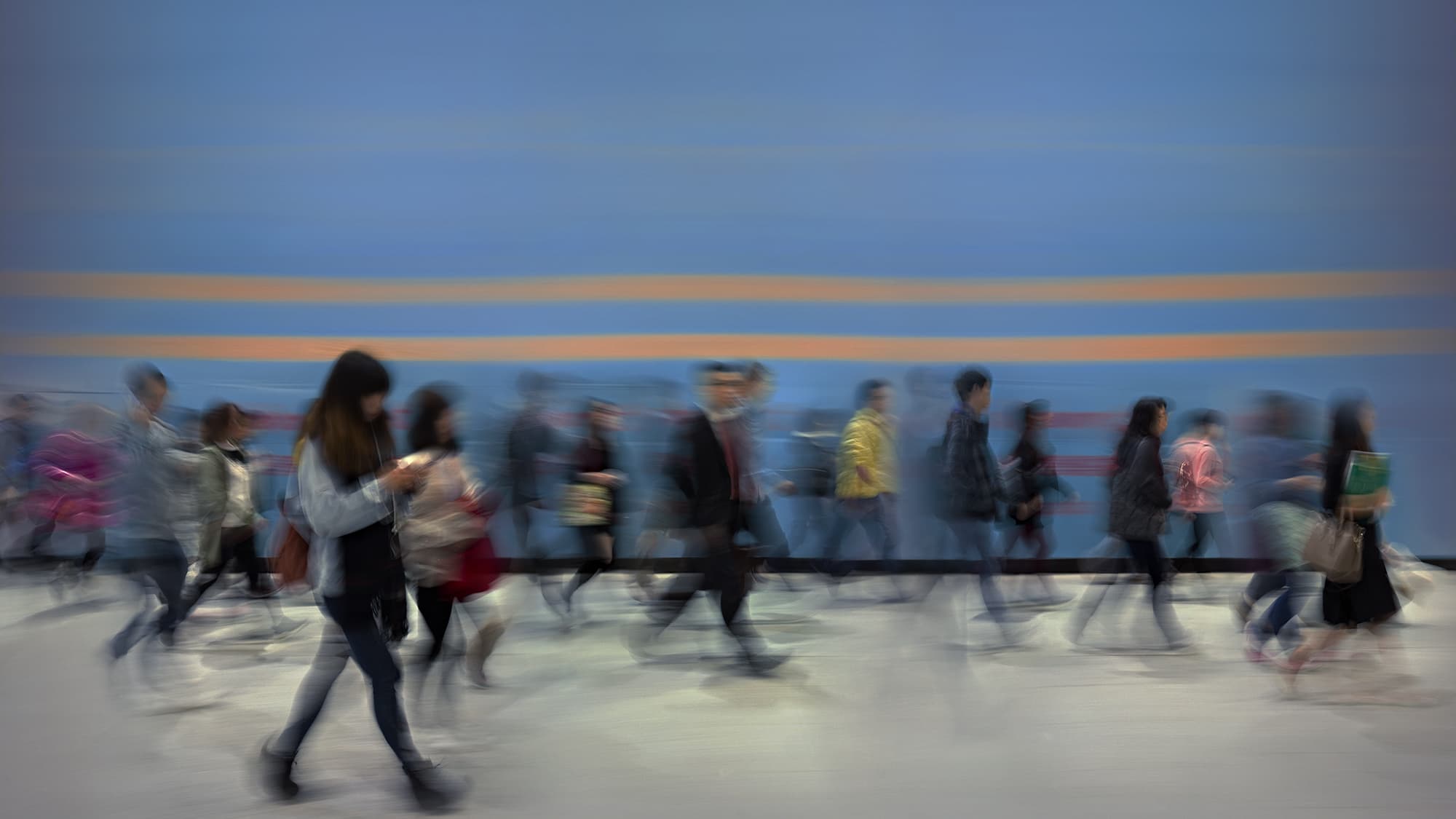 A group of people commuting passing blue wall (motion blurred) in Central District of Hong Kong at dawn.